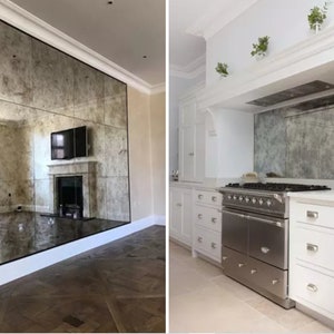 May include: A large wall-mounted antique-style mirror with a distressed, mottled finish composed of multiple rectangular panels. The mirror reflects a room with a fireplace and television, and a kitchen with a stainless steel range and white cabinets.