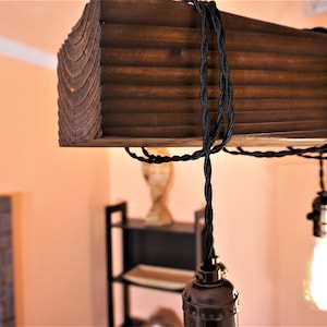 May include: A rustic wooden ceiling light fixture with black electrical cords and exposed Edison bulb sockets.