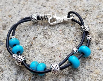 May include: A double-strand leather bracelet with turquoise beads and silver accents. The bracelet has a silver clasp.