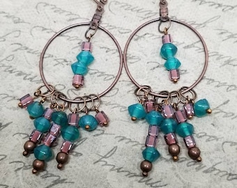 May include: A pair of copper hoop earrings with turquoise and purple glass beads dangling from the bottom. The hoops are connected to the earrings with a copper wire.