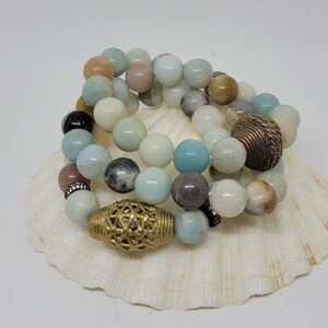 May include: A set of three bracelets made with light blue, green, and brown gemstone beads. The bracelets are accented with gold metal spacers.