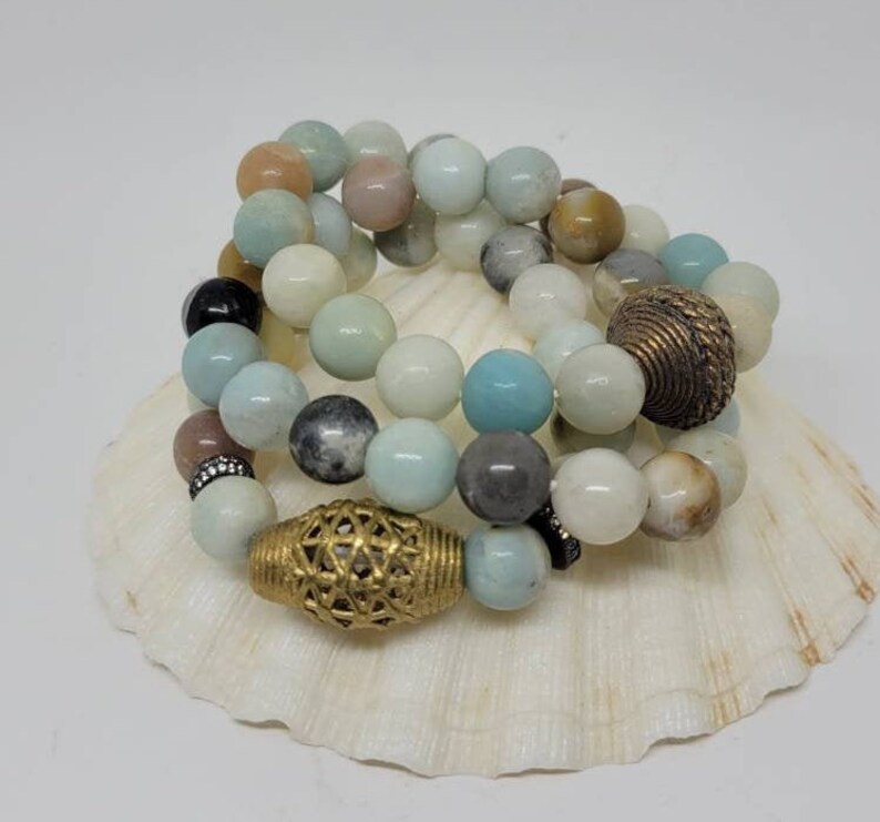 May include: A set of three bracelets made with light blue, green, and brown gemstone beads. The bracelets are accented with gold metal spacers.