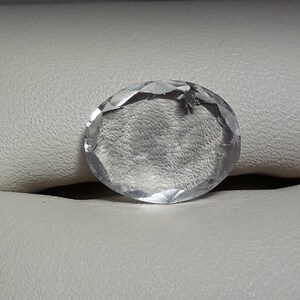 May include: A clear, faceted oval-shaped gemstone with a smooth, polished surface.