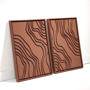 May include: Two rectangular, brown wall art panels with a layered, topographic design. The panels are framed and feature a series of curved, horizontal lines, creating a sense of depth and texture. The artwork is leaning against a white wall.