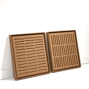 Könnte beinhalten: Zwei braune, rechteckige Tabletts mit einem Raster aus Schlitzen, die in die Oberfläche geschnitten sind. Die Tabletts bestehen aus einem hellbraunen Material und sind vor einem weißen Hintergrund platziert. Die Tabletts sind zur Aufnahme kleiner Gegenstände bestimmt.