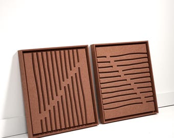 May include: Two brown, square, wooden wall art pieces. One features vertical and angled cut-out lines, the other has horizontal and curved cut-out lines. Both are displayed against a white wall and floor.