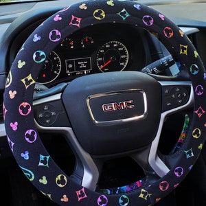 May include: Black steering wheel cover with a colorful Mickey Mouse and Louis Vuitton inspired pattern. The cover is installed on a black steering wheel with a GMC logo.
