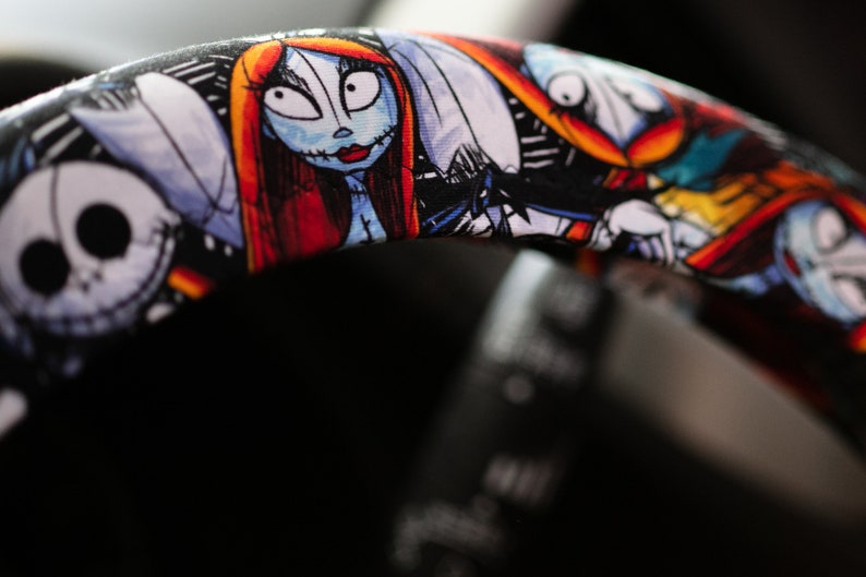 Puede incluir: Una funda para volante negra con un estampado colorido que presenta personajes de la pel&iacute;cula Pesadilla antes de Navidad. Los personajes incluyen a Jack Skellington, Sally y Oogie Boogie.