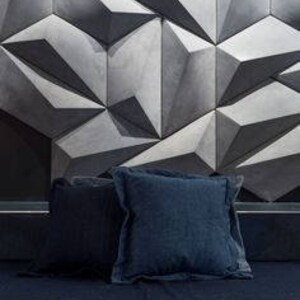 May include: Two navy blue square throw pillows with ruffled edges rest on a dark blue surface. The pillows are in front of a geometric, three-dimensional wall design in shades of gray.