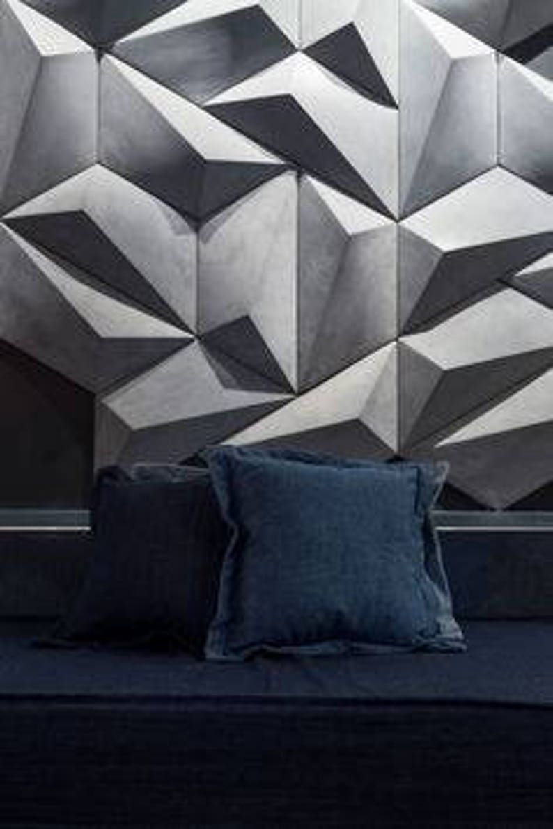 May include: Two navy blue square throw pillows with ruffled edges rest on a dark blue surface. The pillows are in front of a geometric, three-dimensional wall design in shades of gray.