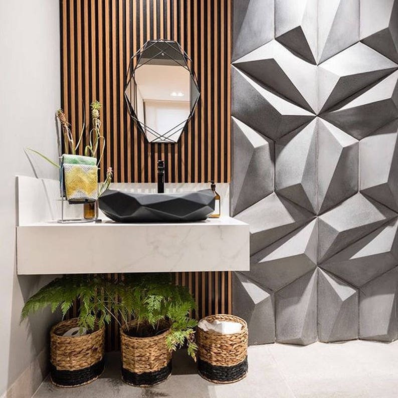 May include: Modern bathroom design featuring a black geometric sink, a black framed mirror, and a textured gray wall. The sink sits on a white countertop with plants in woven baskets below. The background has vertical wood paneling.