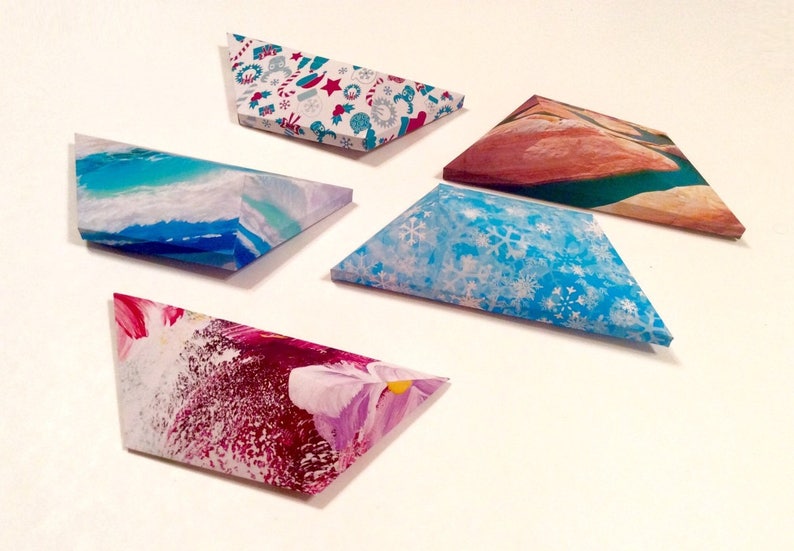 May include: Five triangular gift boxes with various designs. One box has a blue and white winter snowflake pattern. Another features a watercolor ocean scene. The others have abstract floral and holiday patterns. The boxes are arranged on a white surface.