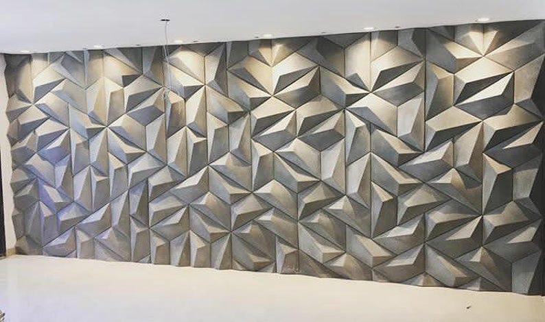 May include: A large wall panel with a geometric, three-dimensional design. The panel is composed of numerous triangular and polygonal shapes in varying shades of gray, creating a textured surface. The wall is illuminated by recessed lighting.