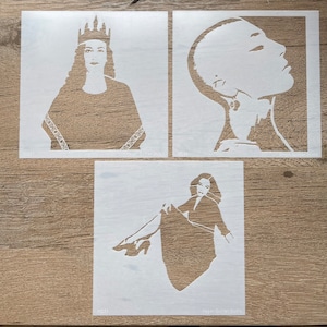 May include: Three white stencils on a wooden surface. The stencils feature portraits of women, including a woman wearing a crown, a woman in profile, and a woman in a seated pose. The bottom stencil has the text "Megan Quinn Studio".