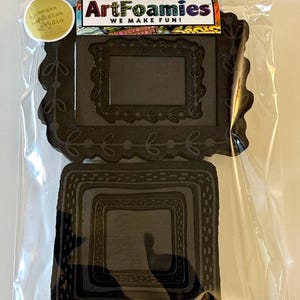 May include: A package containing two black foam frame cutouts. The top frame has a decorative floral design and the text "ArtFoamies WE MAKE FUN!" is visible. A gold sticker with the text "megan quinlan studio" is also visible.