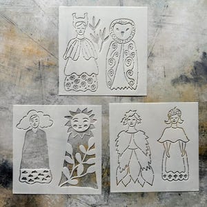 May include: Three square white stencils featuring die-cut line art designs. The top stencil shows a figure and an owl. The bottom left stencil depicts a figure with a cloud head and a sun figure. The bottom right stencil shows two figures.