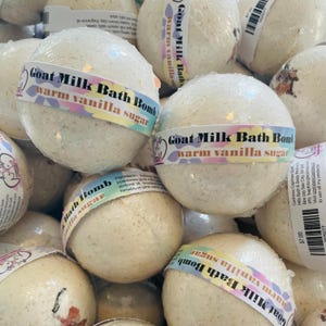 May include: A close-up of a pile of white bath bombs with a label that reads "Goat Milk Bath Bomb warm vanilla sugar".