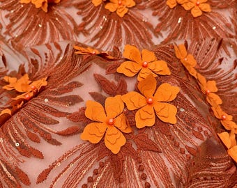 Puede incluir: Una tela transparente con intrincados bordados en tonos cobre y detalles de lentejuelas. El material está adornado con aplicaciones florales naranjas tridimensionales, cada una centrada con una pequeña cuenta naranja, creando textura.