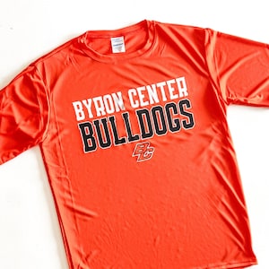 May include: Bright orange athletic t-shirt with the text "BYRON CENTER BULLDOGS" in white and black lettering. The shirt also features a "BC" logo. The shirt is made of a lightweight, breathable material.