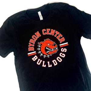 May include: Black t-shirt with a circular graphic featuring the text "BYRON CENTER BULLDOGS" in white and red. The graphic includes a red bulldog head with a spiked collar.