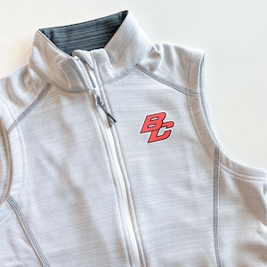 May include: A light gray vest with a full-length zipper and a stand-up collar. The vest features a red and black logo on the chest. The vest has a textured pattern and dark gray stitching.
