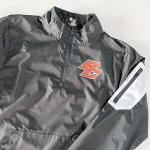 May include: A black windbreaker jacket with a zipper closure and a white and gray sleeve. The jacket has a red and white logo that says "BC" on the front.