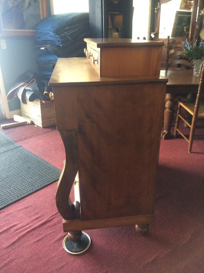 May include: A wooden dresser with three drawers and a top shelf. The dresser is a light brown color and has a curved front.