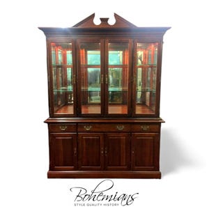 May include: A dark brown wooden hutch with glass doors and shelves. The top section has glass doors, and the bottom has drawers and cabinet doors. The word "Bohemians" is written in cursive at the bottom, with "Style Quality History" below it.