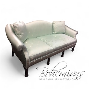 May include: A light blue, tufted sofa with a curved back and wooden legs. The sofa has two pillows and a subtle floral pattern.