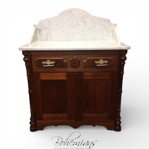 May include: A dark wood antique cabinet with a white marble top and backsplash. The cabinet has two drawers with brass handles and two doors. The word "Bohemians" is written in cursive at the bottom of the image. The cabinet is a vintage piece of furniture.