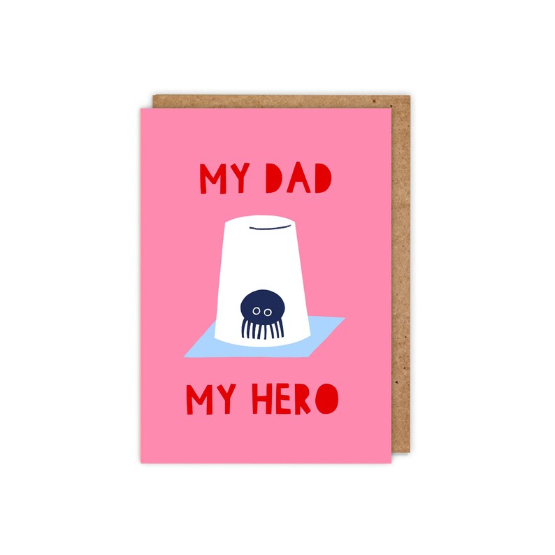 Puede incluir: Una tarjeta rosa con el texto "My Dad My Hero" en rojo. Una taza blanca con un pulpo azul dentro est&aacute; ilustrada en la tarjeta.