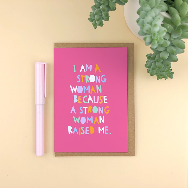 Puede incluir: Tarjeta rosa con el texto "Soy una mujer fuerte porque una mujer fuerte me cri&oacute;." El texto est&aacute; en letras coloridas y divertidas.
