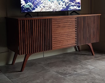 May include: A dark wood entertainment unit with a slatted design and a flat top. A flat screen television is sitting on top of the entertainment unit. The television is displaying a screen saver of an underwater scene with colourful fish and coral.