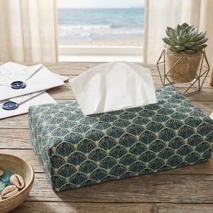 Peut inclure: Un distributeur de mouchoirs rectangulaire avec un motif de ventilateur bleu sarcelle et or. Des mouchoirs blancs dépassent du dessus. La boîte est posée sur une table en bois avec d'autres objets décoratifs.