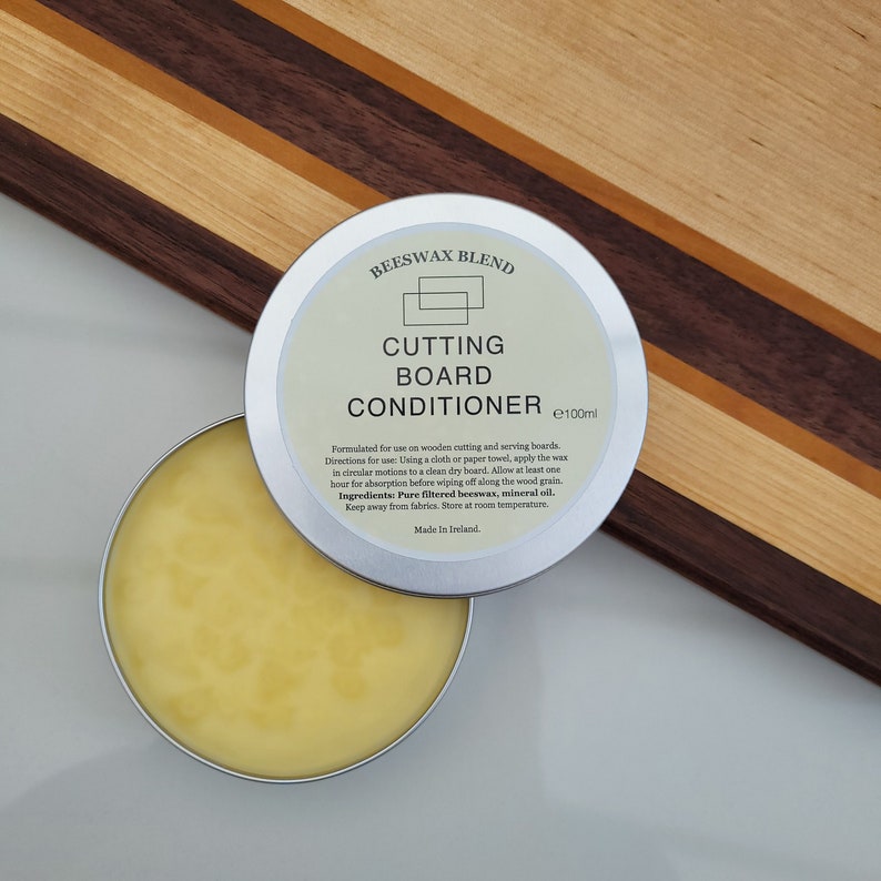 May include: A silver tin containing yellow wax. The tin is labelled "Beeswax Blend Cutting Board Conditioner 100ml". The label also includes directions for use and ingredients.