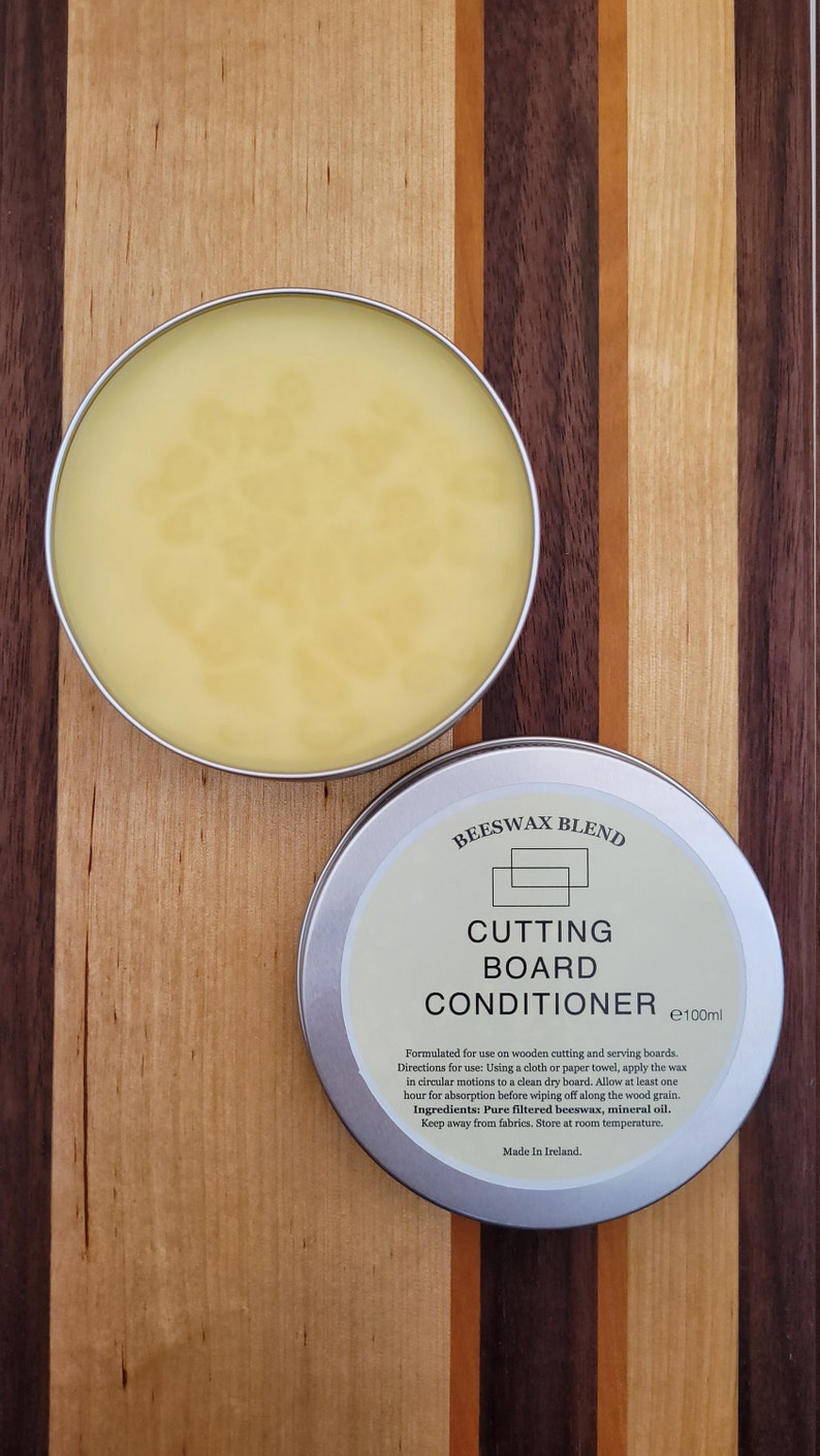 May include: A silver tin of beeswax blend cutting board conditioner with a yellow wax inside. The tin is labelled "Beeswax Blend Cutting Board Conditioner e100ml". The label also includes instructions for use and ingredients: Pure filtered beeswax, mineral oil. Made in Ireland.