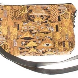 May include: A small, brown and gold tapestry bag with a black leather strap. The bag has a geometric pattern with eyes and triangles.