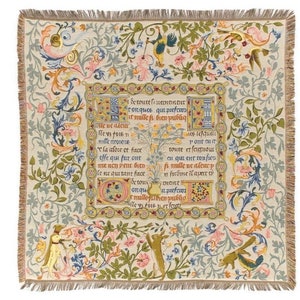 Op de afbeelding: Een tapijt met een crèmekleurige achtergrond en een centraal paneel met een middeleeuwse tekst in het Frans. De tekst wordt omringd door een decoratieve rand van bloemen en wijnstokken in tinten groen, geel, roze en blauw. Het tapijt is omlijst door een franjerand.