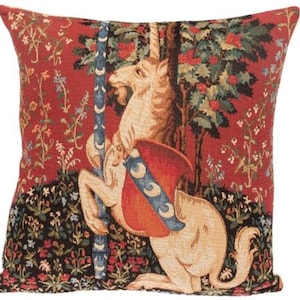 May include: A red, black, and white tapestry pillow featuring a unicorn standing on its hind legs with a shield and a tree behind it.