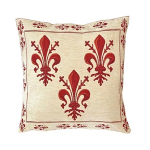 May include: A square throw pillow with a cream-colored background and a red embroidered design of three fleur-de-lis.