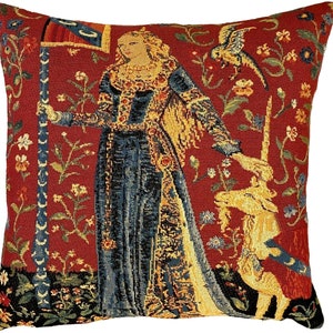May include: A tapestry-style throw pillow featuring a woman in a blue and gold gown holding a unicorn. The background is a red floral pattern.