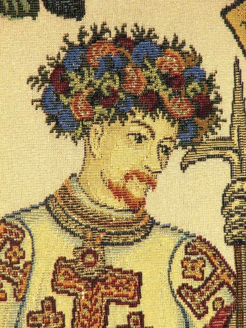 May include: Close-up of a tapestry depicting a man wearing a crown of leaves and flowers. He is wearing a tunic with a cross on the front. The tapestry is made of woven threads in shades of brown, gold, red, blue, and green.