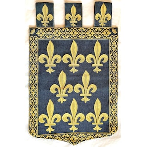 May include: A blue tapestry wall hanging with a gold fleur-de-lis pattern. The tapestry has a scalloped bottom edge and three gold tassels at the top.