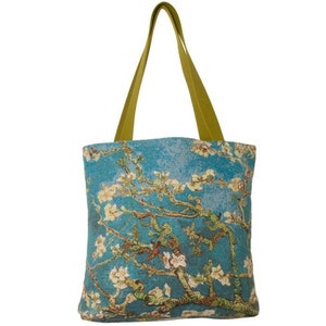 Pode incluir: Uma bolsa tote azul com uma alça verde e uma imagem impressa de um ramo de amendoeira em flor. A imagem é uma reprodução de uma famosa pintura de Vincent van Gogh.
