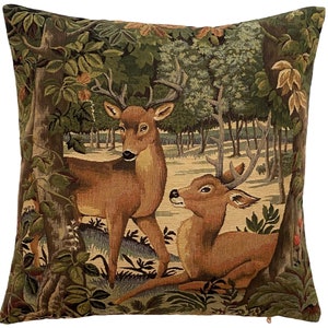 May include: A tapestry pillow featuring a brown deer with antlers standing in a forest setting with green trees and foliage. A second deer is lying down in the foreground.