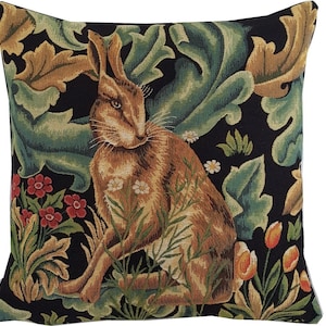 Könnte beinhalten: Ein schwarzes und grünes Wandteppichkissen mit einem braunen Kaninchen, das in einem Blumenfeld sitzt. Das Kaninchen ist umgeben von grünen Blättern und Blumen in Rot-, Orange- und Weißtönen.