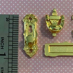 May include: Gold-toned metal door hardware set, including a door knob, door knocker, mailbox, and key. The set is approximately 1 inch in size.