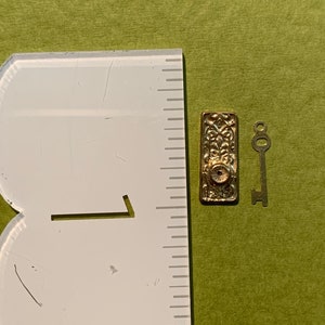May include: A gold-toned key and a decorative door knob with an ornate design. The key is about 1 inch long and the door knob is about 1.5 inches tall.