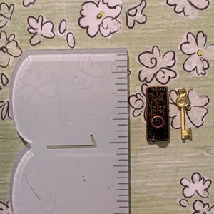 May include: A miniature key and keyhole charm set. The keyhole is made of metal with a brown and gold finish. The key is gold metal.