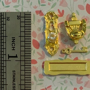 May include: Miniature gold-colored door hardware set, including a doorknob with a clear gem, a door knocker, a key, and a mail slot. The ruler next to the hardware shows the items are approximately 1 inch in size.